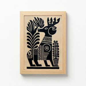 May include: Black and white folk art print of a stylized deer with large antlers, surrounded by stylized plants. The artwork is framed in a light wood frame. The deer has geometric patterns on its body and is set against a beige background.