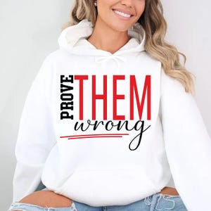 May include: White hooded sweatshirt with the text "PROVE THEM wrong" in black and red. The word "PROVE" is stacked vertically on the left, while "THEM" is in large red letters. "wrong" is in a cursive font.