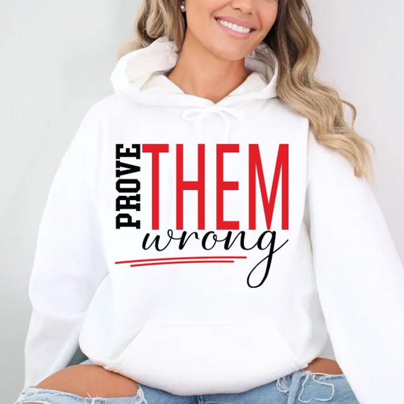 May include: White hooded sweatshirt with the text "PROVE THEM wrong" in black and red. The word "PROVE" is stacked vertically on the left, while "THEM" is in large red letters. "wrong" is in a cursive font.