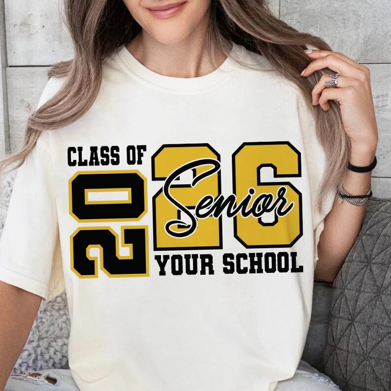 Pode incluir: Camiseta creme com o texto "CLASS OF 2026 Senior YOUR SCHOOL" em letras pretas e douradas. A camiseta &eacute; de estilo casual, adequada para a formatura.