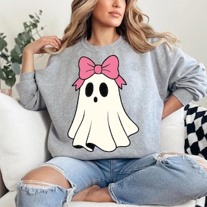 K&ouml;nnte beinhalten: Hellgraues Sweatshirt mit einem Cartoon-Geist mit rosa Schleife. Der Geist ist wei&szlig; mit schwarzen Augen und einem kleinen Mund. Das Sweatshirt hat lange &Auml;rmel und einen Rundhalsausschnitt.