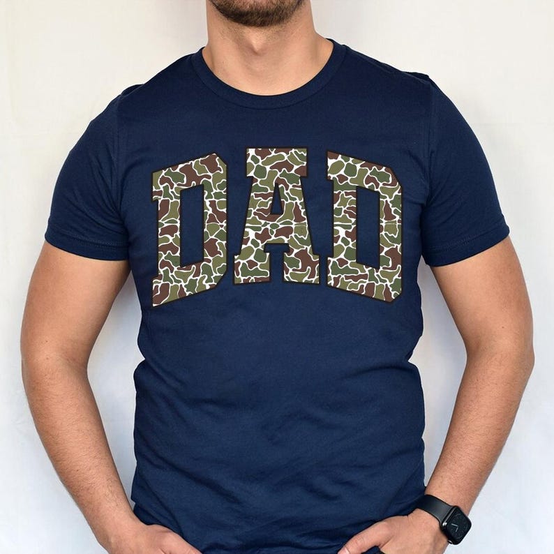May include: A navy blue t-shirt with a large "DAD" graphic in a camouflage pattern.