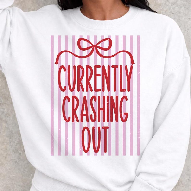 May include: White sweatshirt with a red bow and the text "CURRENTLY CRASHING OUT" in red. The text is set against a background of vertical pink and white stripes.