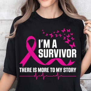 以下が含まれることがあります： ピンクのリボンと白い文字で「I'M A SURVIVOR」と書かれた黒いTシャツ。ピンクの蝶と「THERE IS MORE TO MY STORY」の文字も表示されています。心拍ラインが一番下にあります。