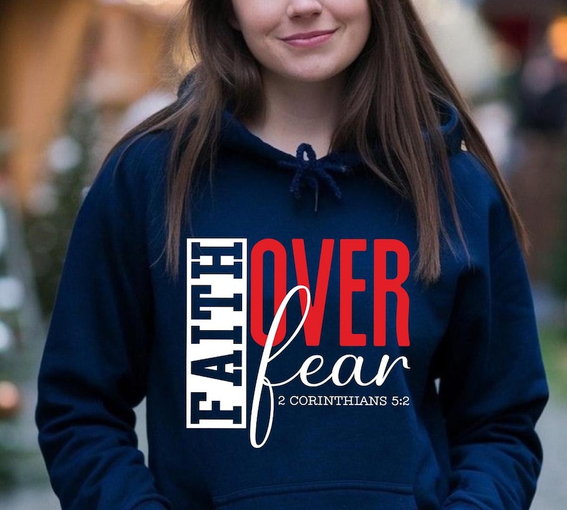 May include: Navy blue hooded sweatshirt with the words "FAITH OVER FEAR" in white and red lettering. The text "2 Corinthians 5:2" is below the word "fear". The sweatshirt has a drawstring and a front pocket.