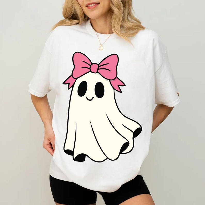 K&ouml;nnte beinhalten: Wei&szlig;es T-Shirt mit einem Cartoon-Geist-Design. Der Geist hat eine rosa Schleife, schwarze Augen und einen l&auml;chelnden Mund. Der Geist wird mit einem wei&szlig;en Laken mit schwarzem Rand dargestellt.