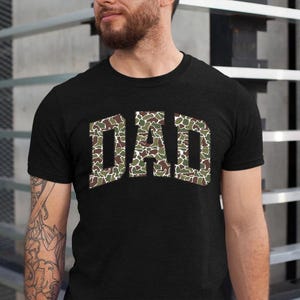 May include: Black t-shirt with the word "DAD" in a camouflage pattern.