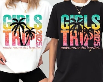 May include: Two t-shirts, one white and one black, featuring a colorful graphic. The graphic includes the words "GIRLS TRIP 2025" with palm trees and the phrase "make memories together". The shirts are short-sleeved.