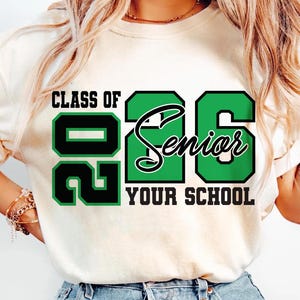Pode incluir: Camiseta creme com o texto "CLASS OF 2026 Senior YOUR SCHOOL" em verde e preto. O design apresenta o ano de 2026 em uma fonte em negrito e em bloco, com "Senior" em it&aacute;lico.