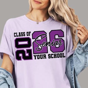 Pode incluir: T-shirt lil&aacute;s claro com o texto "CLASS OF 2026 Senior YOUR SCHOOL" em preto e roxo. A t-shirt tem gola redonda e mangas curtas.