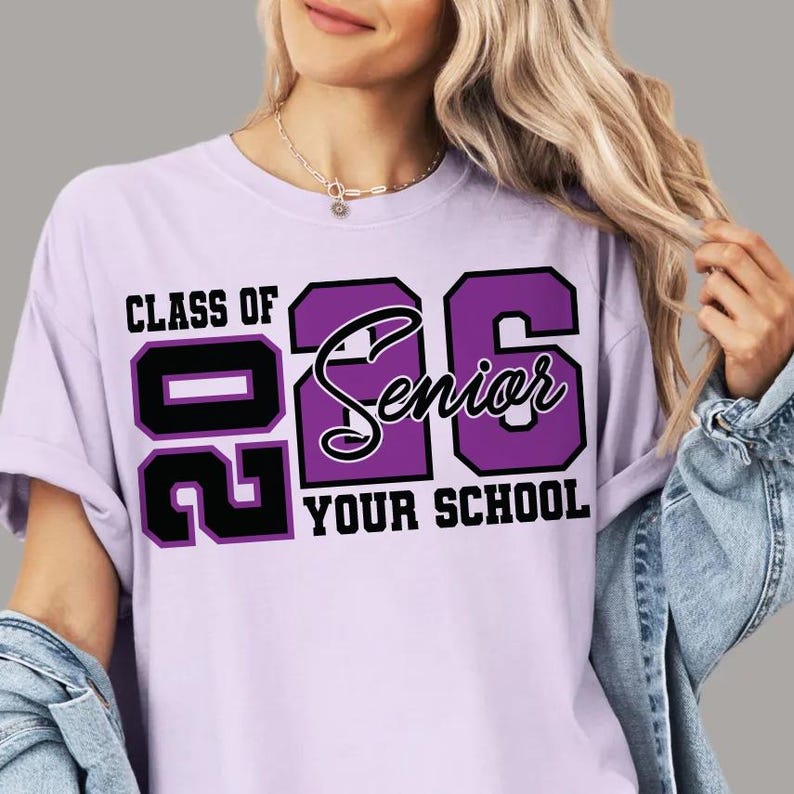 Pode incluir: T-shirt lil&aacute;s claro com o texto "CLASS OF 2026 Senior YOUR SCHOOL" em preto e roxo. A t-shirt tem gola redonda e mangas curtas.