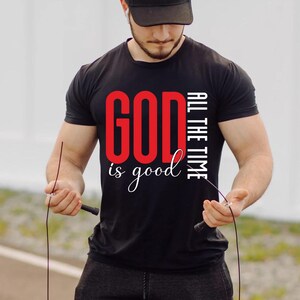 May include: Black crew neck t-shirt with the text "GOD is good ALL THE TIME" in red and white. The person in the image is wearing a black cap and holding a jump rope.