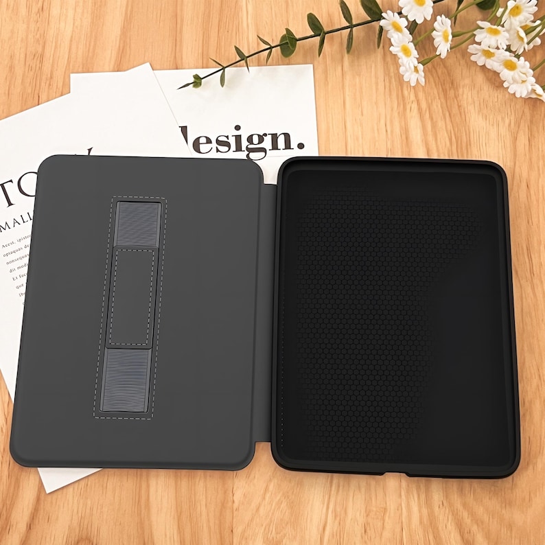 May include: A black and gray tablet case with a built-in stand. The case is open and the stand is extended. The case has a textured interior and a smooth exterior. The case is designed to protect a tablet from scratches and bumps.