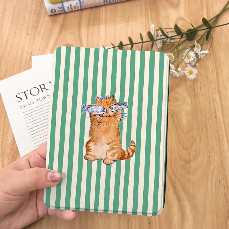 May include: A green and white striped book cover with a cartoon illustration of a cat holding two fish in front of its eyes. The cat is orange and white and has a happy expression.