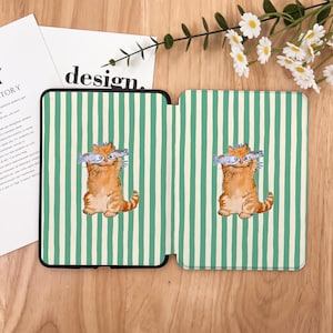 May include: A green and white striped kindle cover with a cartoon orange cat holding two fish in its mouth. The cat is on both sides of the cover.