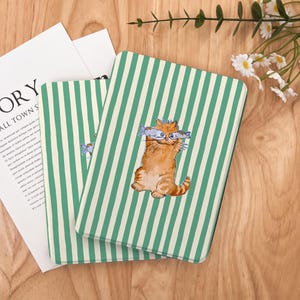 May include: Two green and white striped book covers with a cartoon illustration of a cat holding two fish in its mouth. The cat is orange and white with a black nose and whiskers.