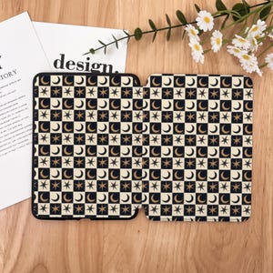 May include: Two black and beige tablet cases with a celestial pattern of moons and stars in a checkerboard design. The word "design" is visible on a white paper in the background. The cases are open, revealing the interior.