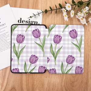 May include: A phone case and a tablet case with a purple tulip pattern on a white and light purple gingham background. The cases are black and the design includes green stems and leaves. The word "design" is visible on a white paper.