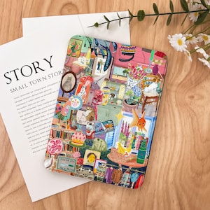 May include: A colorful, rectangular decorative item with a collage of images, including a cat portrait, framed art, and various objects. The text "STORY SMALL TOWN STOR" is visible on a white paper. The item is on a wooden surface.