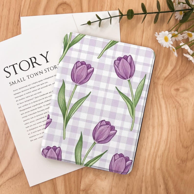 May include: A rectangular case featuring a purple tulip floral pattern on a light purple and white checkered background. The case is on a wooden surface with a white paper and the text "STORY SMALL TOWN STOR".
