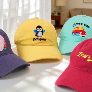 May include: Four baseball caps in different colours are shown. A purple cap has a heart with "LOVE MOM" embroidered. A yellow cap features a penguin design. A light blue cap has a car design and the words "I love car". A red cap has "Baby's name" embroidered.