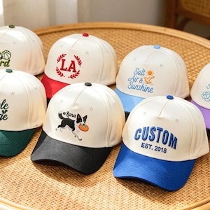Könnte beinhalten: Eine Auswahl an Baseballkappen mit weißen Kronen und farbigen Schirmen. Jede Kappe hat gestickte Designs und Texte, darunter "Play Hard", "LA", "Maple Ridge", "Luna", "Salt Air & Sunshine", "Plant Parent" und "CUSTOM EST. 2018".