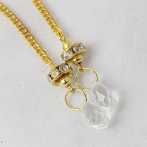 Puede incluir: Un par de cadenas de oro con colgantes de cristal transparente. Cada colgante tiene un anillo de oro y una peque&ntilde;a pieza redonda de oro con diamantes de imitaci&oacute;n transparentes.