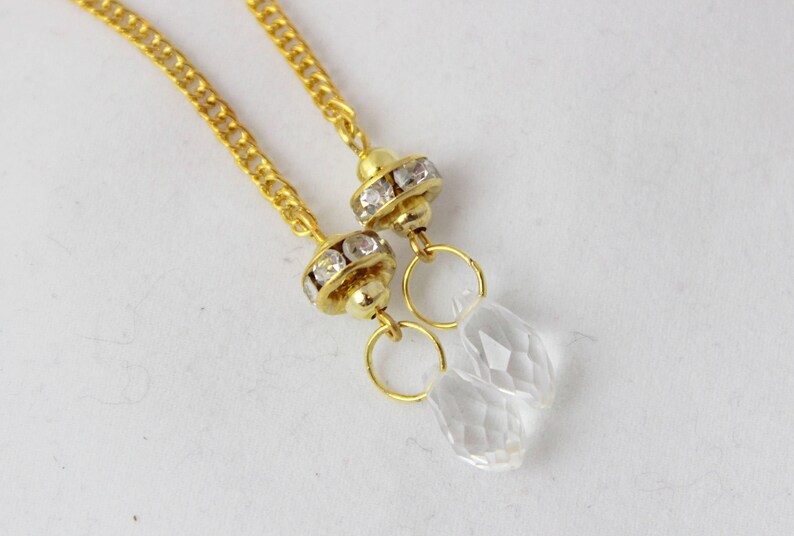Puede incluir: Un par de cadenas de oro con colgantes de cristal transparente. Cada colgante tiene un anillo de oro y una peque&ntilde;a pieza redonda de oro con diamantes de imitaci&oacute;n transparentes.