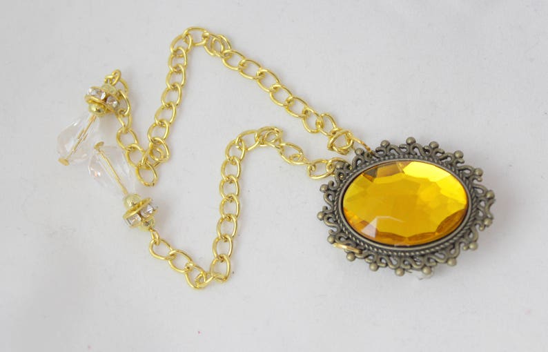 Puede incluir: Un collar de cadena dorada con un gran colgante de forma ovalada, de piedra preciosa de color &aacute;mbar, engastado en un marco adornado de color bronce.