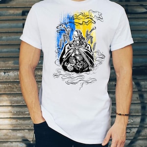 Pode incluir: T-shirt branca com uma ilustração a preto e branco de uma figura com trigo e espadas, contra um fundo de pinceladas azuis e amarelas. O design evoca um guerreiro ou figura histórica.