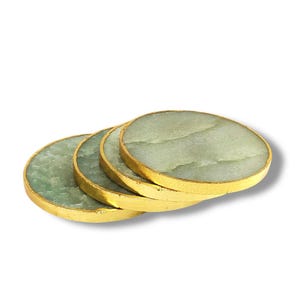 May include: Set of four green agate coasters with gold trim. The coasters are round and have a natural stone look.