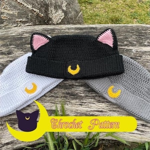 May include: A black crochet beanie with cat ears and a yellow crescent moon emblem. Two other beanies, one gray and one light gray, are also visible, each with a yellow crescent moon. The image includes a yellow banner with the text "Chrochet Pattern".