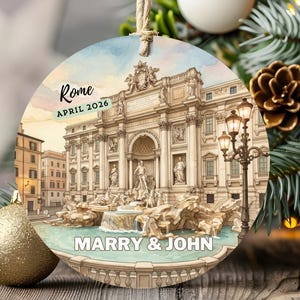May include: Circular Christmas decoration with a watercolour image of the Trevi Fountain in Rome. The ornament has the text "Rome April 2026" and "Marry & John". It is suspended from a Christmas tree.