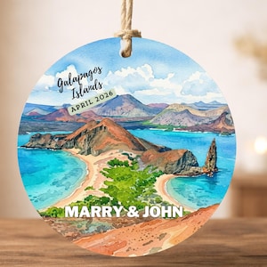 May include: Circular ornament with a watercolour painting of the Galapagos Islands. The image shows a beach, mountains, and ocean. Text on the ornament reads "Galapagos Islands APRIL 2026" and "MARRY & JOHN". A beige string is attached for hanging.