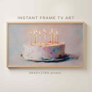 May include: A framed digital art print of a birthday cake with lit candles. The cake is white with colorful accents, and the candles have glowing flames. The text "INSTANT FRAME TV ART" is at the top.