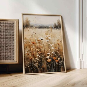 K&ouml;nnte beinhalten: Gerahmter Kunstdruck, der ein Feld mit Wildblumen in Orange, Wei&szlig; und Gelb zeigt. Das Kunstwerk zeigt hohes Gras und einen sanften, neutral get&ouml;nten Himmel. Der Rahmen ist helles Holz.