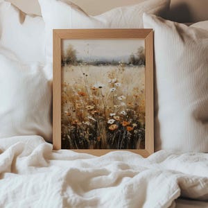 May include: A rectangular framed wall art piece featuring a landscape painting of a wildflower meadow. The artwork displays a field of white and orange flowers with tall grasses in muted earth tones, set against a soft, hazy horizon line.