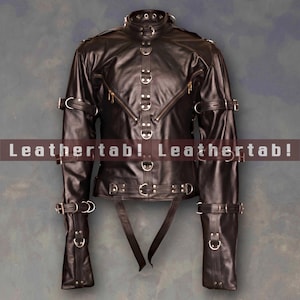 Può includere: Giacca in pelle nera con più cinturini, fibbie e anelli metallici. La giacca ha un collo alto, cerniere e maniche lunghe. Il testo "Leathertab! Leathertab!" è stampato sull'immagine.