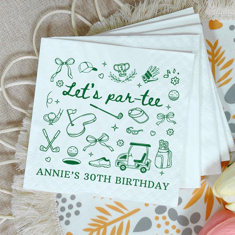 May include: White paper napkins with a green golf-themed design. The napkins feature golf-related illustrations and the text "Let's par-tee" and "ANNIE'S 30TH BIRTHDAY". The napkins are stacked on top of each other.