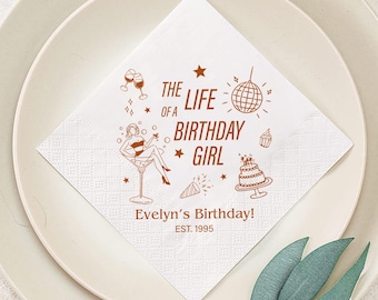 Könnte beinhalten: Quadratische weiße Papierserviette mit braunen Illustrationen und Text. Das Design umfasst eine Frau in einem Martini-Glas, eine Discokugel, einen Kuchen und den Text "THE LIFE OF A BIRTHAY GIRL" und "Evelyn's Birthday! EST. 1995".