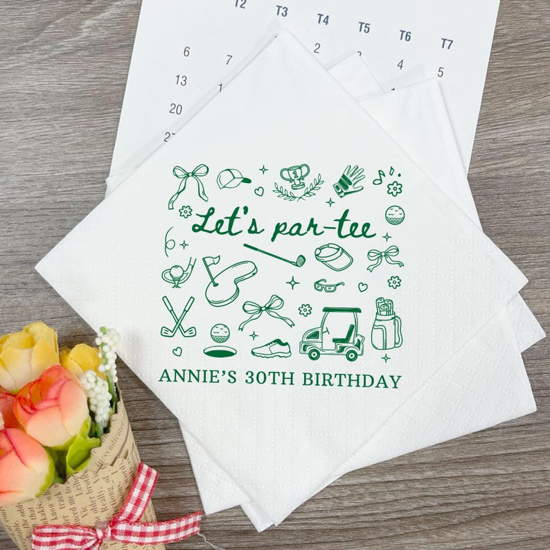 May include: White square paper napkins with a green golf-themed design. The napkins feature golf-related illustrations and the text "Let's par-tee" and "ANNIE'S 30TH BIRTHDAY". A calendar is in the background.