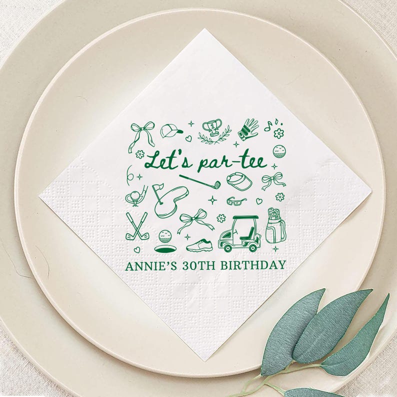May include: White square paper napkin with a green golf-themed design. The napkin features the text "Let's par-tee" and "Annie's 30th Birthday". The design includes golf clubs, balls, a golf cart, and other golf-related icons.