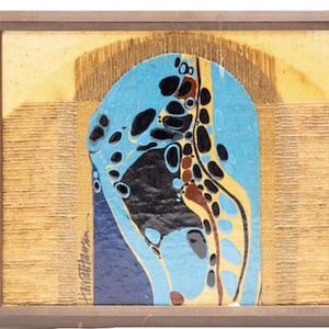 May include: Abstract art piece in a wooden frame. The artwork features a central blue shape with black and yellow details, set against a textured gold background. The artist's signature is visible on the lower left.