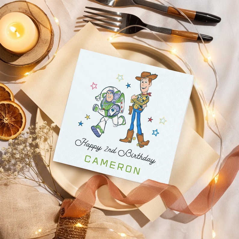 Puede incluir: Una tarjeta de cumplea&ntilde;os blanca con ilustraciones de Buzz Lightyear y Woody, rodeada de estrellas de colores. La tarjeta dice "Happy 2nd Birthday CAMERON" en escritura negra y verde. La tarjeta est&aacute; sobre un plato con una cinta y cubiertos.
