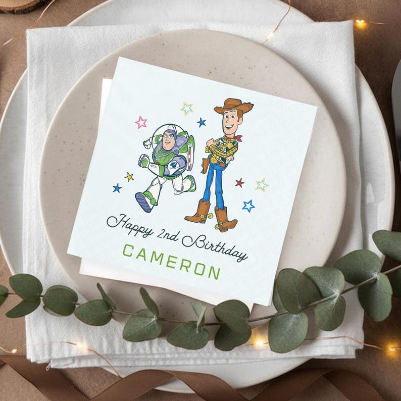 Puede incluir: Tarjeta de cumplea&ntilde;os cuadrada con Buzz Lightyear y Woody de Toy Story, con el texto "Happy 2nd Birthday CAMERON" en verde y negro. La tarjeta est&aacute; colocada sobre una servilleta blanca y un plato beige, con vegetaci&oacute;n decorativa.