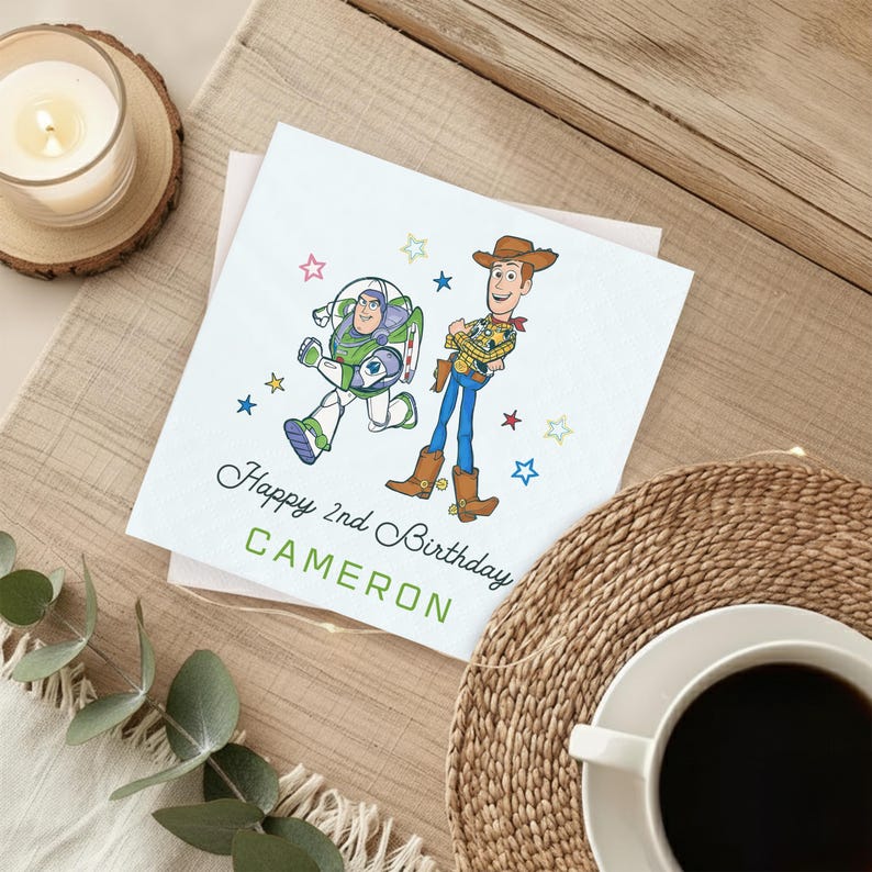 Puede incluir: Tarjeta de cumplea&ntilde;os blanca con los personajes de dibujos animados Buzz Lightyear y Woody. La tarjeta dice "Happy 2nd Birthday CAMERON" en texto verde, rodeada de ilustraciones de estrellas de colores. La tarjeta est&aacute; sobre una superficie de madera con una vela y una taza de caf&eacute;.