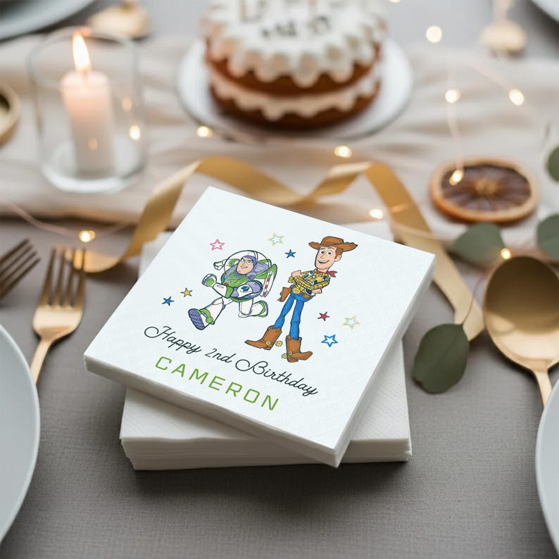 Puede incluir: Servilletas de papel blancas con ilustraciones de Buzz Lightyear y Woody de Toy Story. El texto "Happy 2nd Birthday" y el nombre "Cameron" est&aacute;n impresos en verde y negro. Las servilletas est&aacute;n apiladas sobre una mesa.
