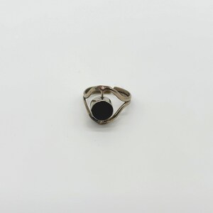 May include: A silver ring with a black circular stone set in the center. The ring has a unique, wavy design on the band. The ring is displayed against a white background.