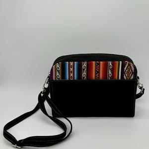 May include: Black crossbody bag with a colorful woven fabric panel across the top. The panel features a geometric pattern in shades of red, orange, blue, and purple. The bag has a long, adjustable strap.