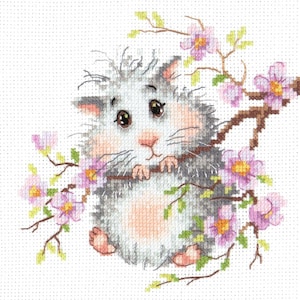 Op de afbeelding: Kruissteekontwerp van een pluizige grijze kat die een tak met roze bloemen vasthoudt. De kat heeft grote bruine ogen, een roze neus en roze poten. De bloemen zijn lichtroze van kleur.